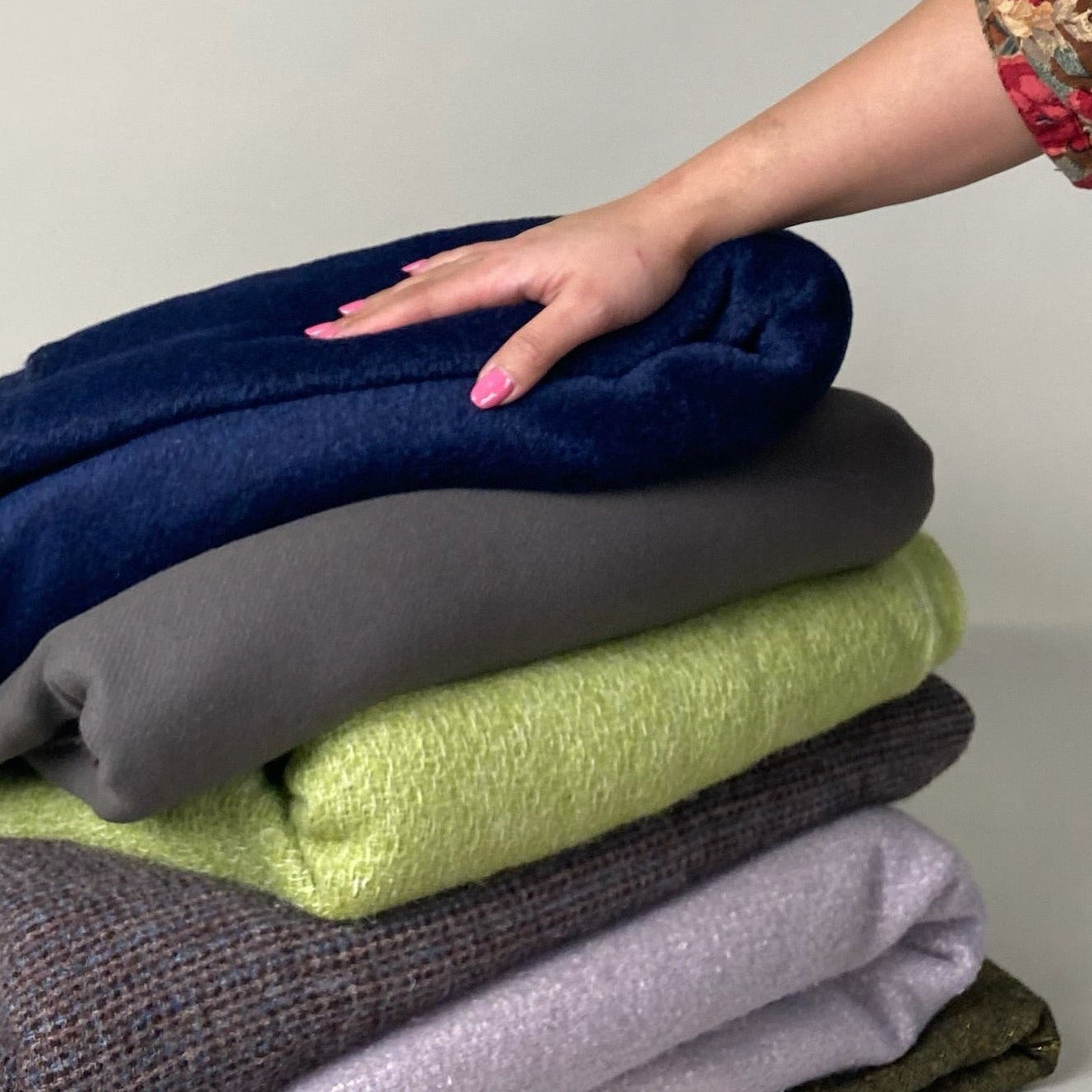 Stack of folded cloths with a hand reaching towards them on a neutral background